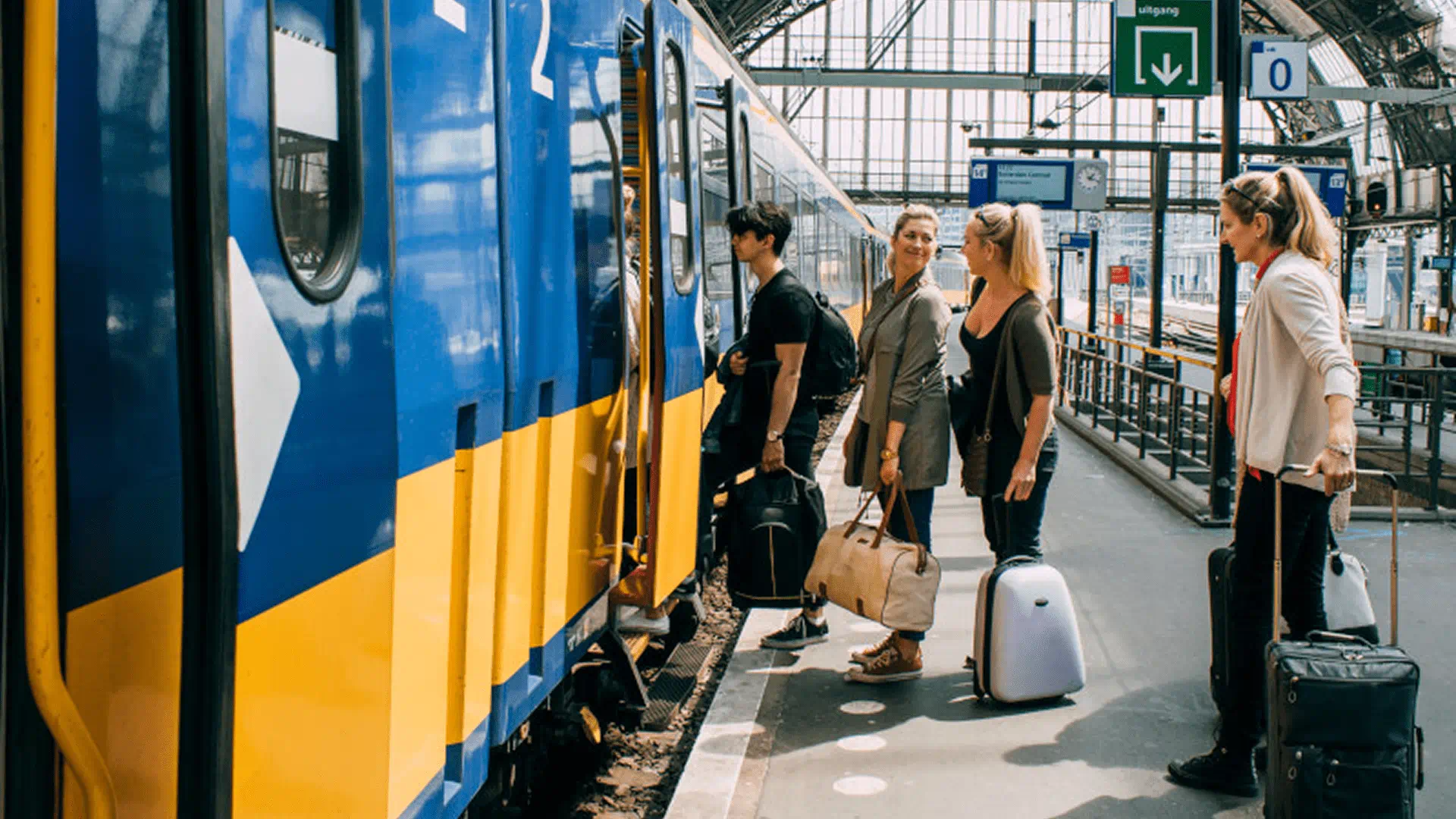 Three people stand next to a train, surrounded by their luggage, awaiting departure.