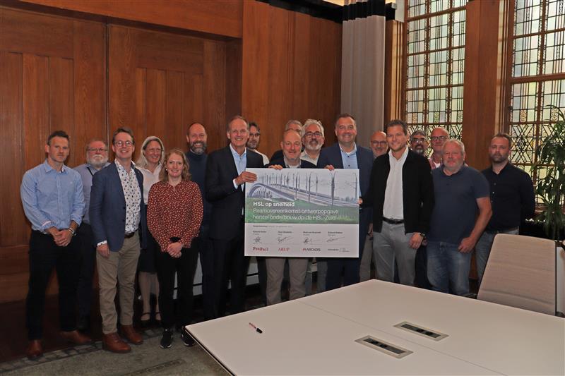 A diverse group of people stands in front of a large board, engaged in discussion or presentation.