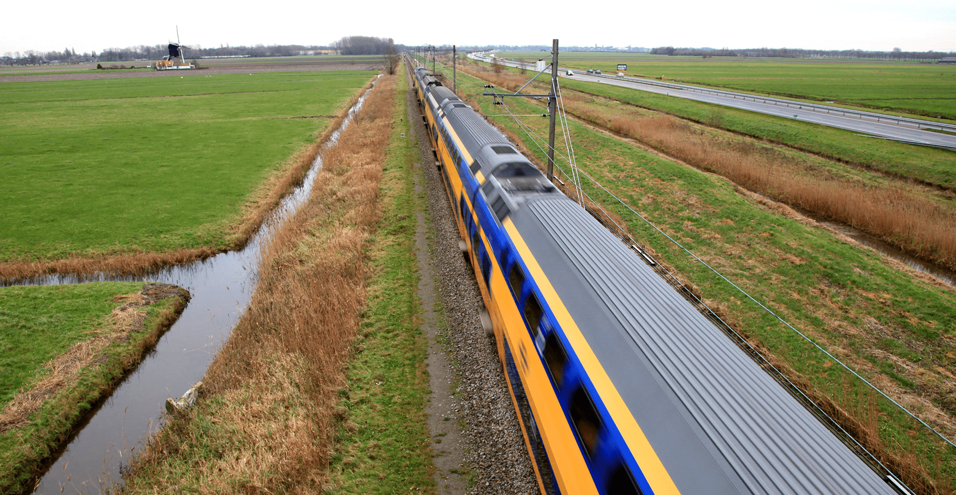 Fast passenger train traveling through open countryside and agricultural fields.
