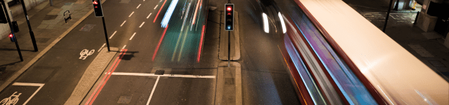 A bustling city street illuminated by streetlights, with blurred lights and cars moving in the night.
