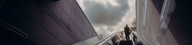 A person going up an escalator, using the handrail for support.