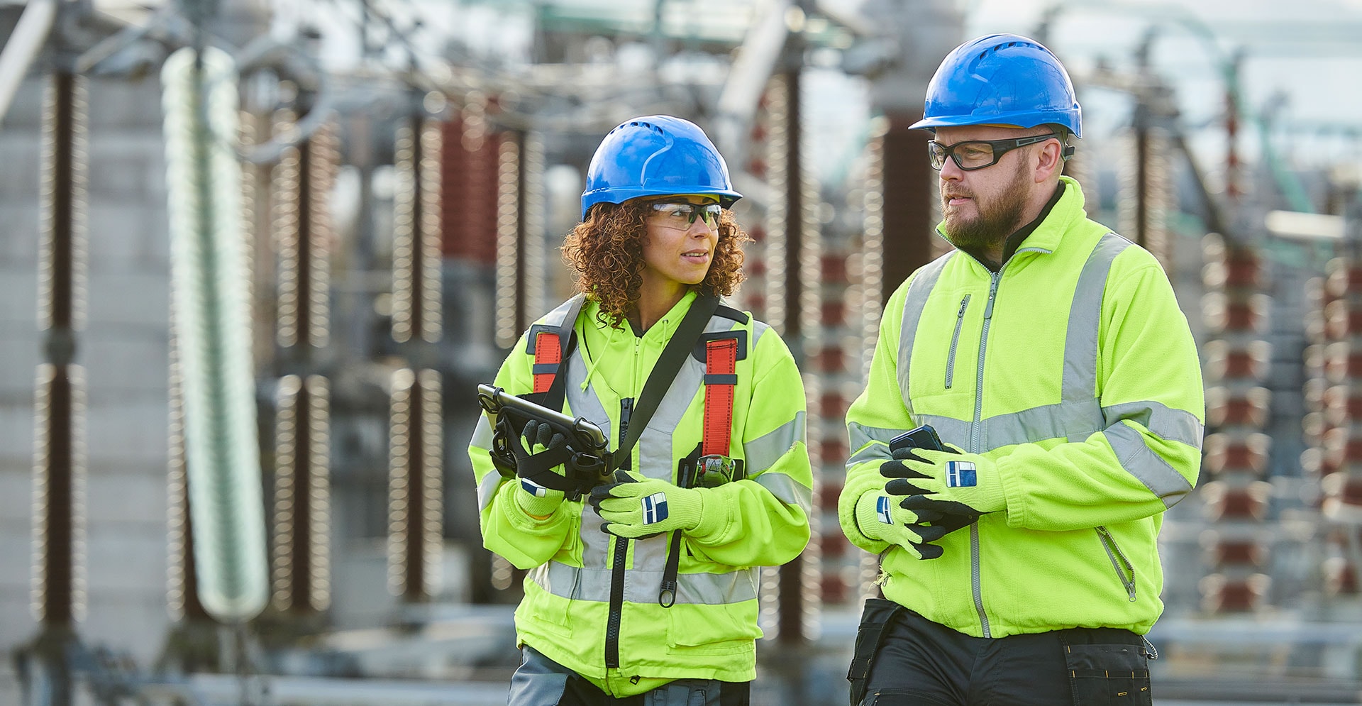 Two individuals in safety gear stand beside a power plant, highlighting safety measures in an industrial environment