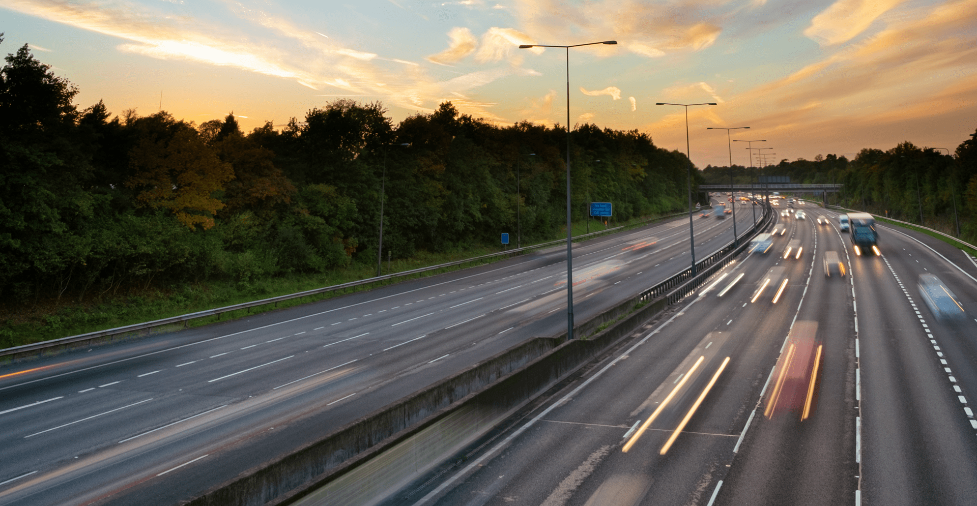 A highway at sunset with cars driving, casting long shadows and vibrant colors across the sky.