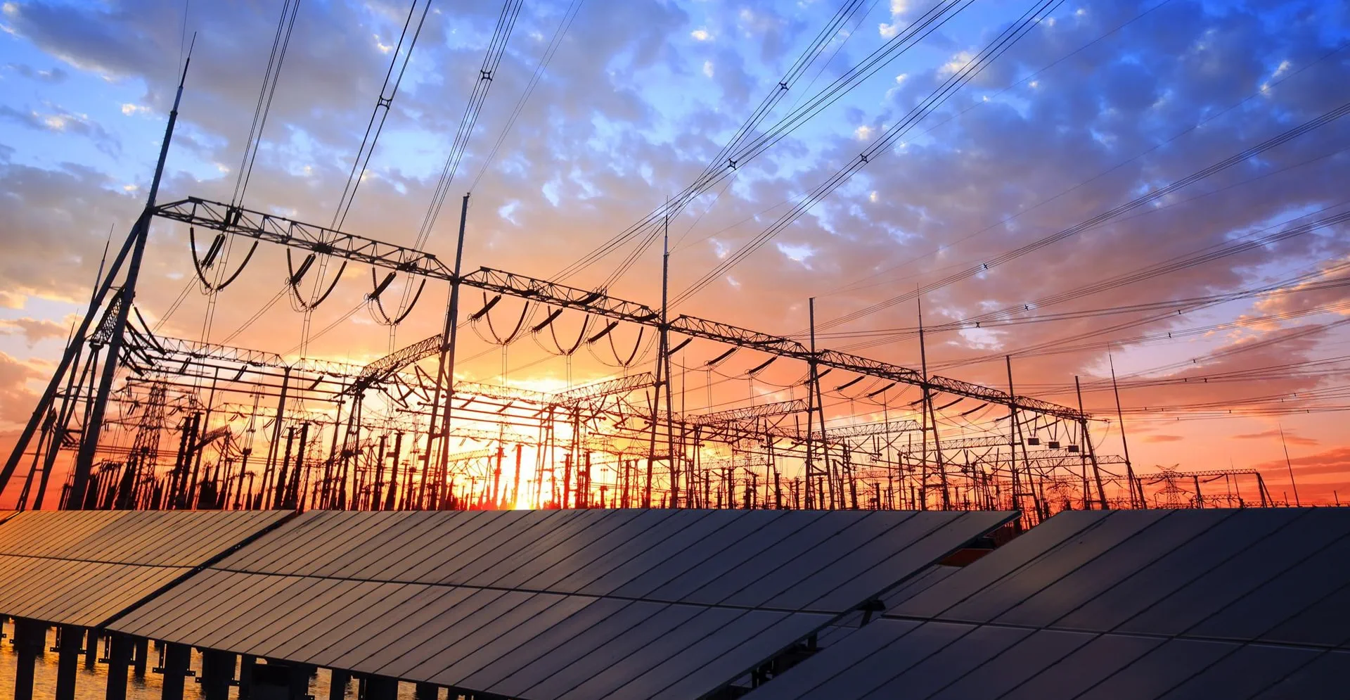 Solar panels and power lines silhouetted against a vibrant sunset sky, showcasing renewable energy in a serene landscape.