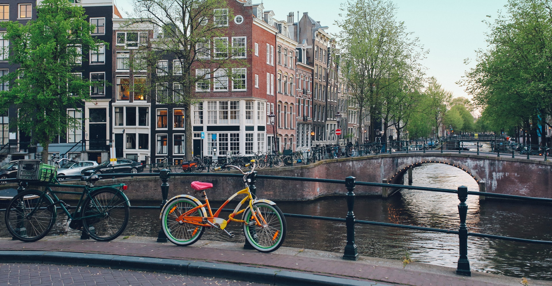 A bicycle rests on a bridge beside a tranquil canal, with reflections of the surroundings in the water.