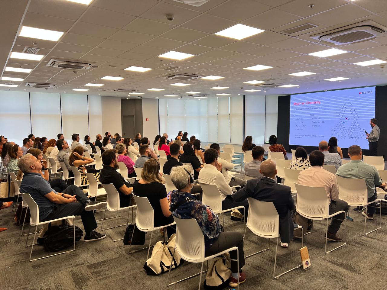 A large group of individuals seated in chairs within a spacious room, engaged in discussion or presentation.