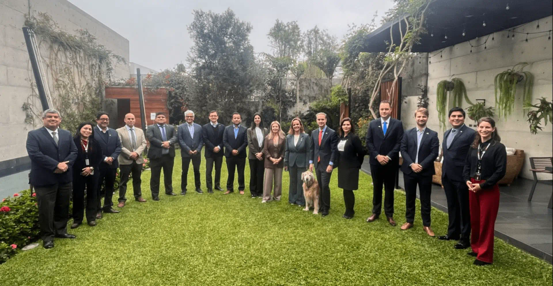 A group of professionally dressed individuals in suits and ties standing together in a lush garden setting.