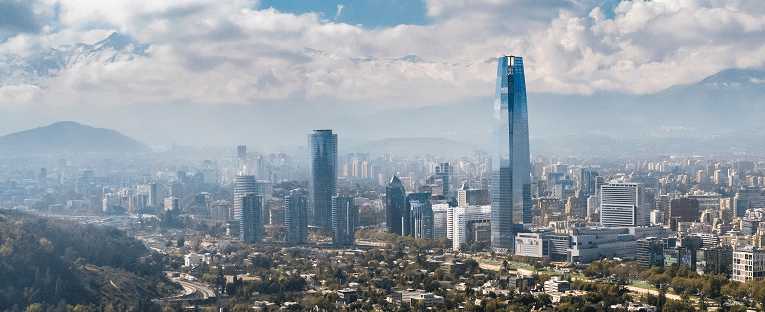 A city skyline featuring tall buildings with majestic mountains rising in the background.
