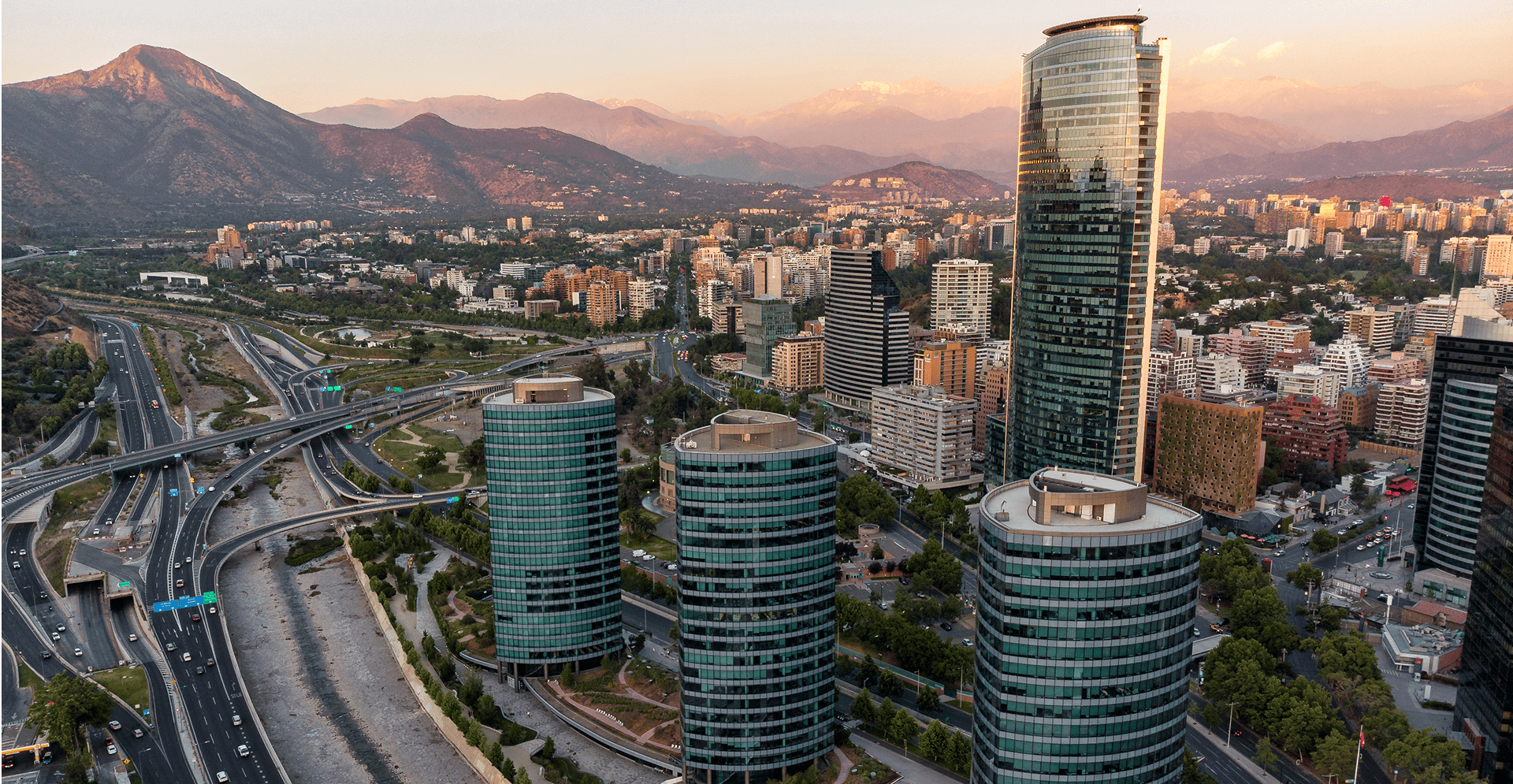 A city skyline featuring numerous tall buildings with majestic mountains rising in the background.