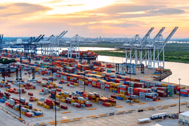 A busy container port filled with colorful shipping containers and towering cranes against a clear blue sky.