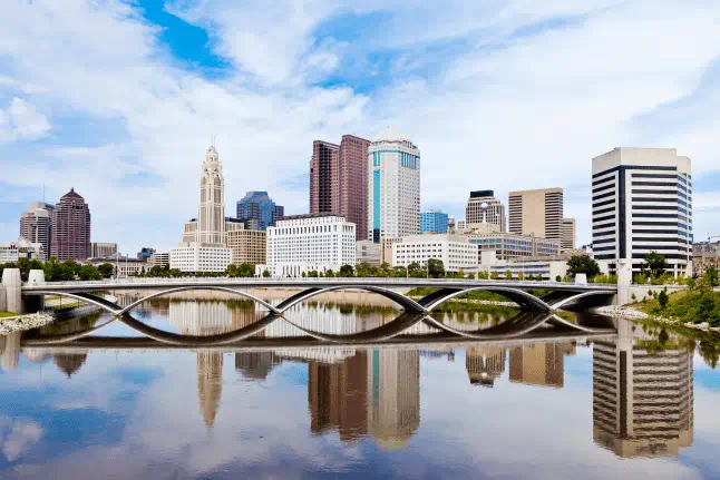 Columbus, Ohio skyline reflected in the Scioto River with the Discovery Bridge in the foreground on a bright day.