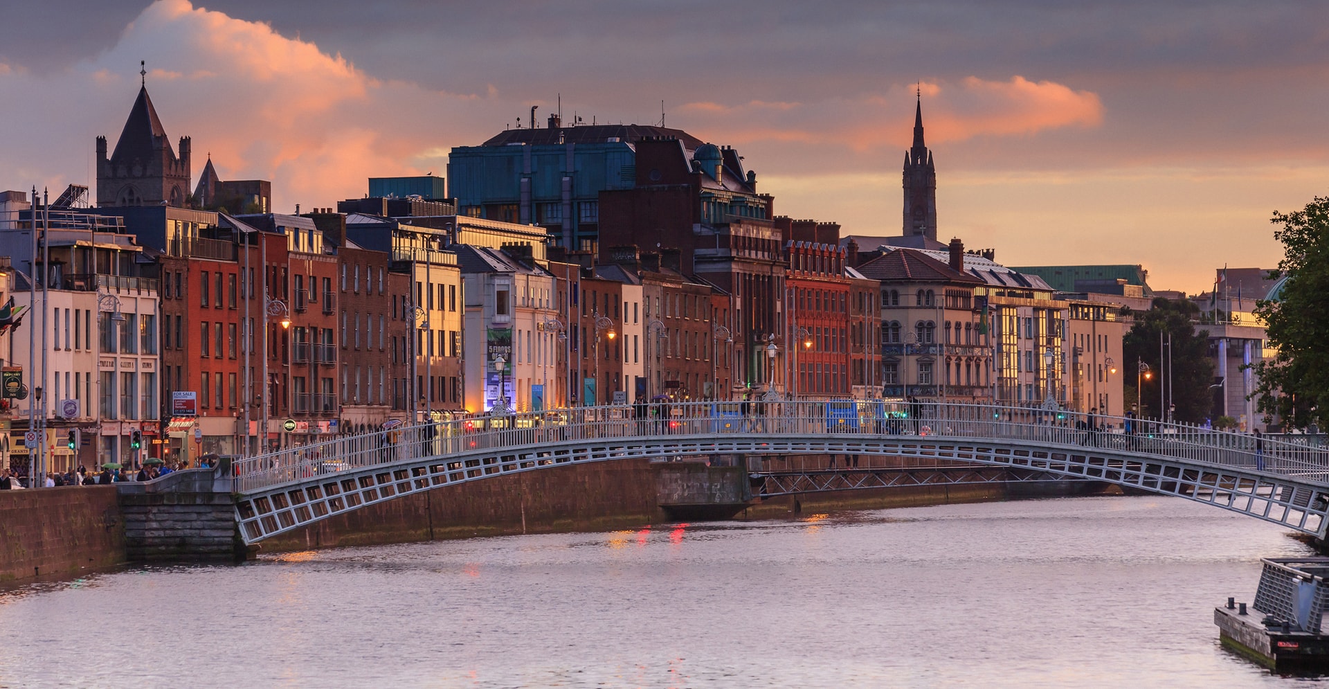 A scenic bridge spans a river, connecting two banks with a sunset background.