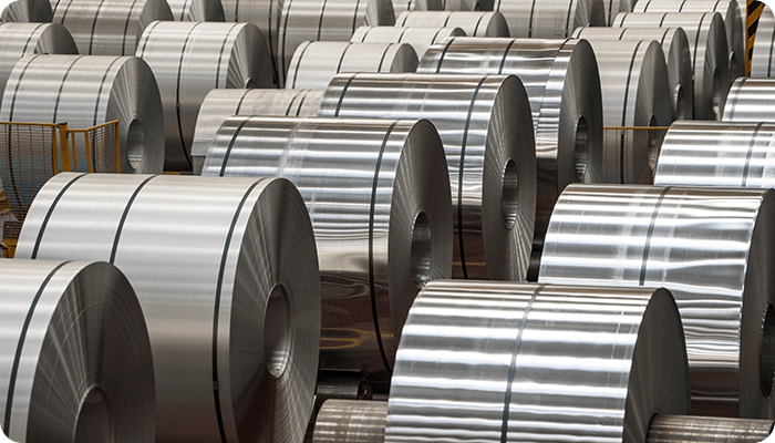 Rows of large, shiny aluminum coils in a warehouse, neatly arranged. The metallic surface reflects light, conveying a sense of industrial precision.