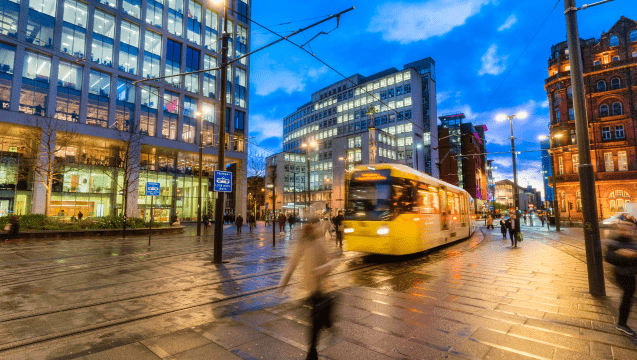 Manchester City centre, City tram approaching with pedestrians walking on the road.