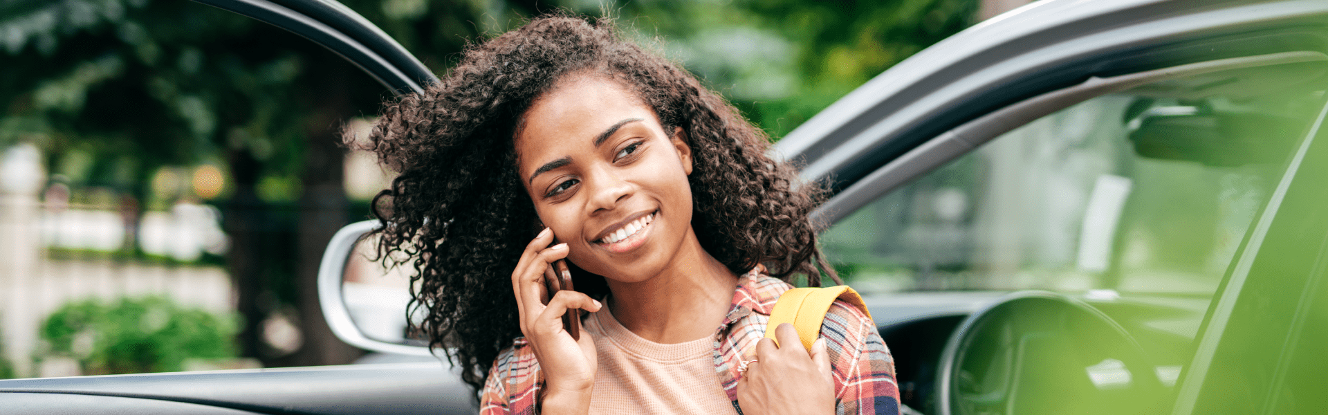 Happy young woman getting out of her car