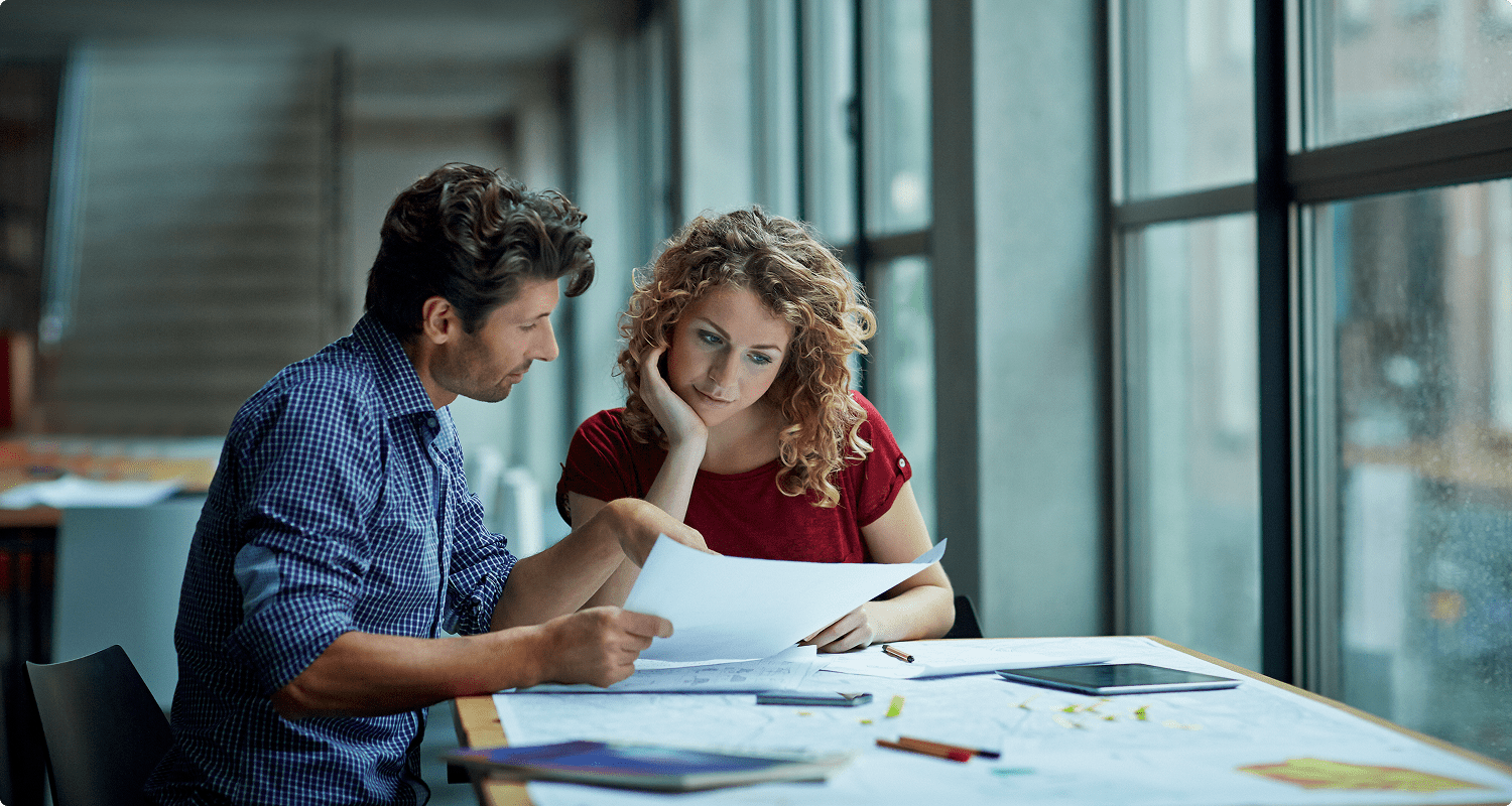 A man and woman at a table, examining papers intently, suggesting a collaborative discussion.