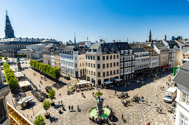 A bustling city square featuring a fountain, with people walking and enjoying the vibrant atmosphere around them.