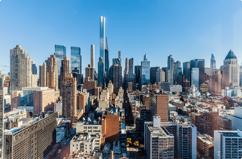 The city skyline viewed from a high-rise, featuring a mix of modern skyscrapers and urban architecture under sunlight.