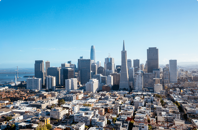 A panoramic view of a city skyline featuring numerous tall buildings against a clear blue sky.