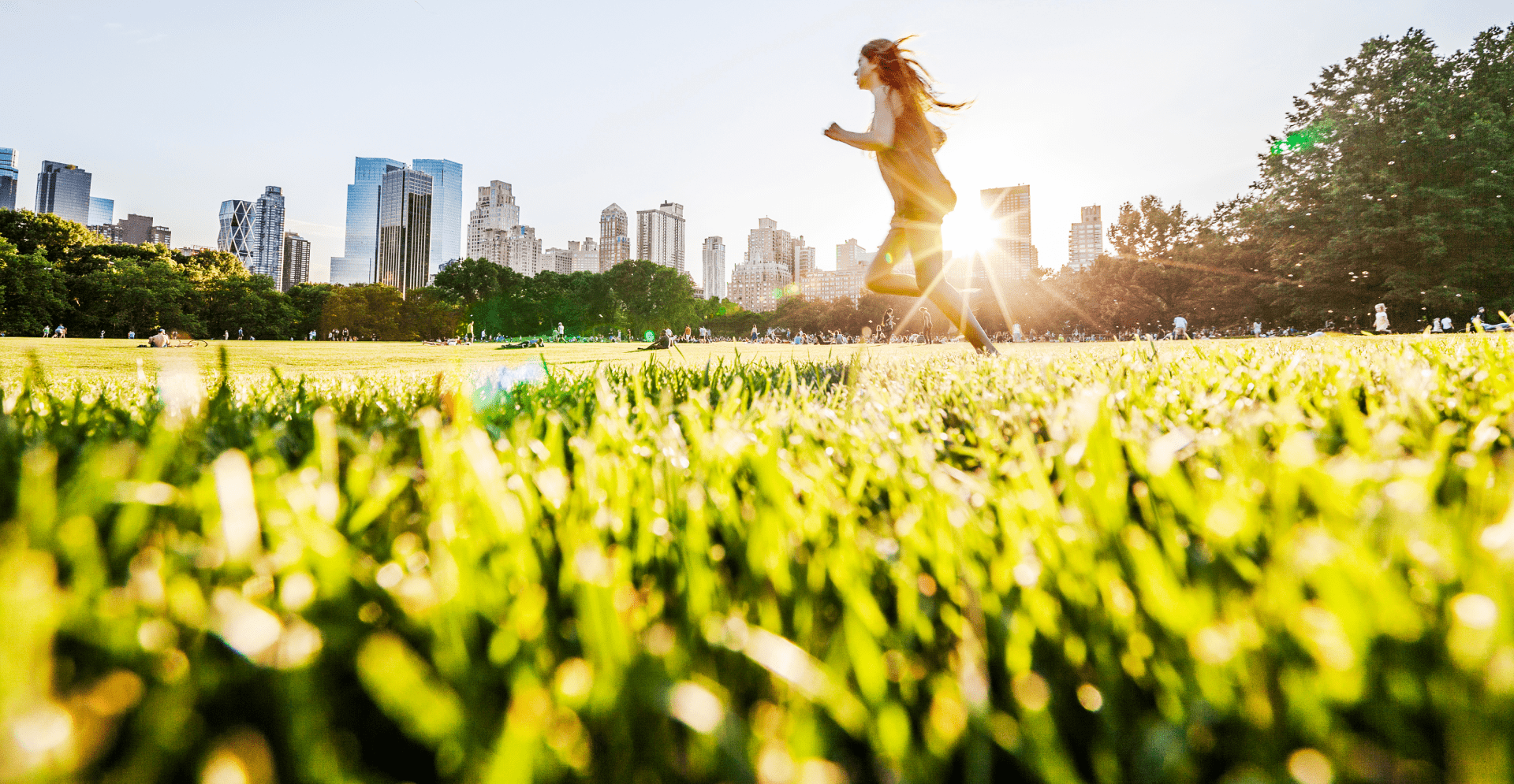 A woman runs through a grassy field, illuminated by the warm glow of the sun in the background.