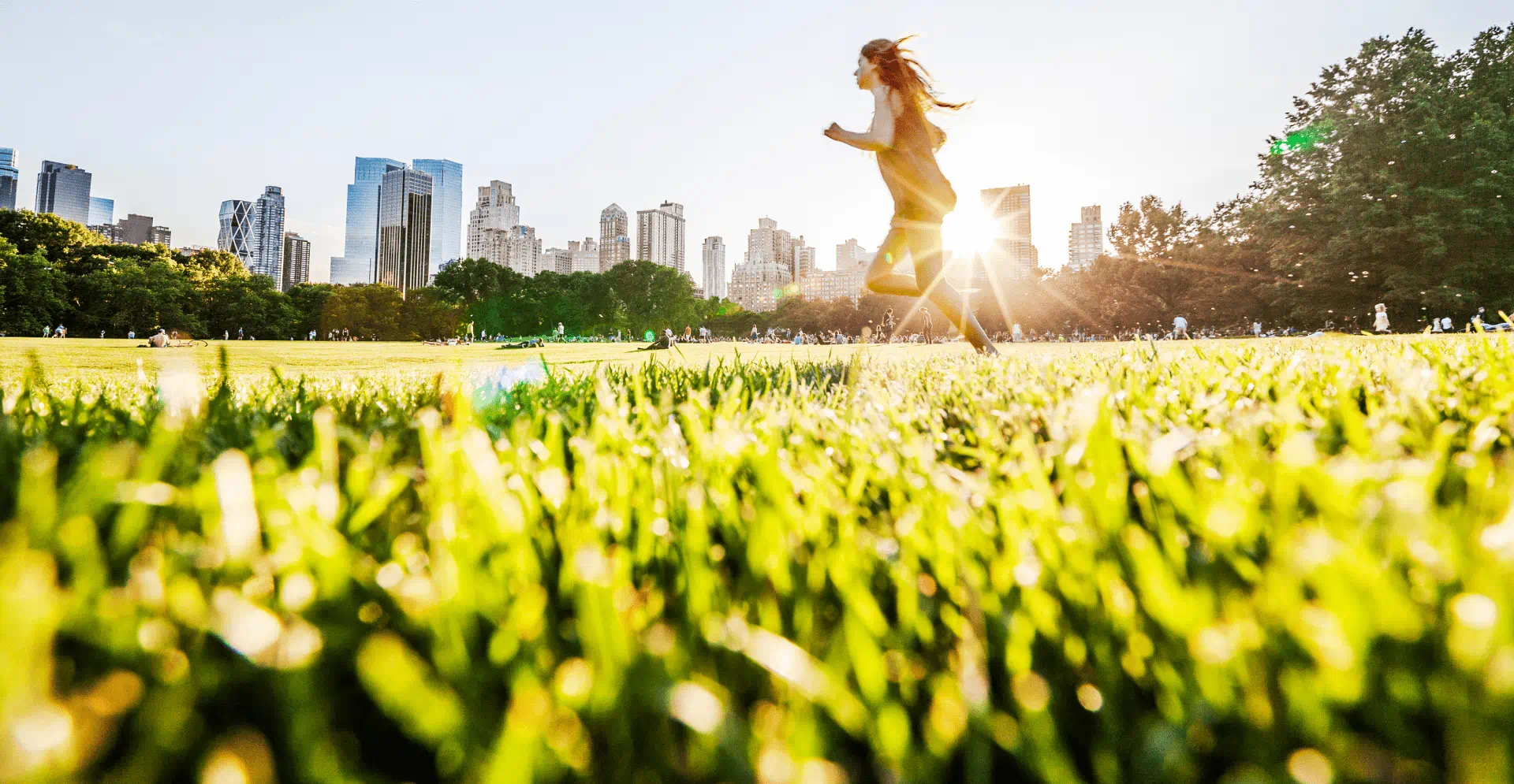 A woman runs through a grassy field, illuminated by the warm glow of the sun in the background.