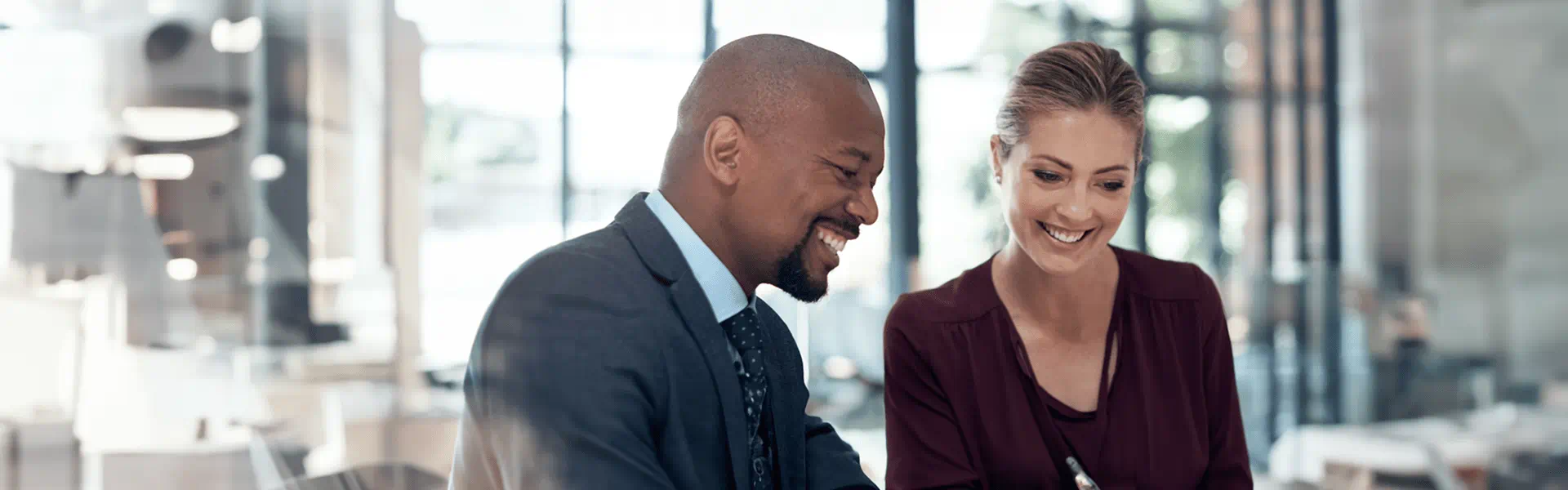 A pair of business individuals seated at a table, actively using a tablet to facilitate their meeting and exchange ideas.