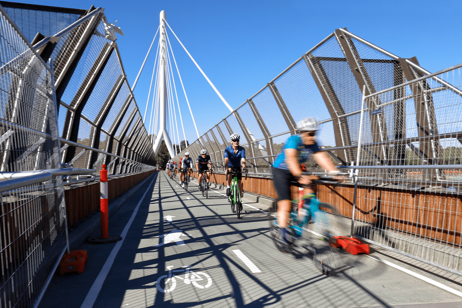 A group of cyclists riding bikes across a bridge on a sunny day, enjoying the outdoors together.
