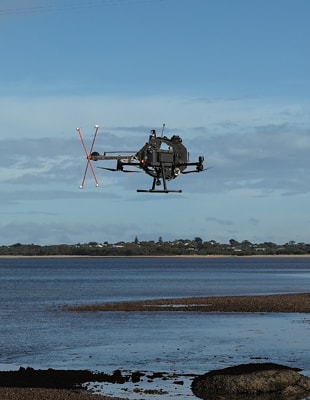 A drone hovers above a calm body of water, reflecting the sky and surrounding landscape.