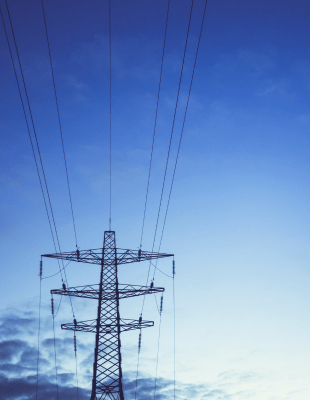 High voltage power lines and electricity towers silhouetted against a clear blue sky, showcasing energy infrastructure.