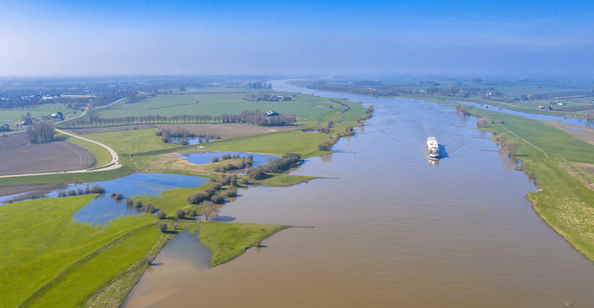 Scenic view of a boat sailing down a tranquil river, with trees lining the banks under a sunny sky.