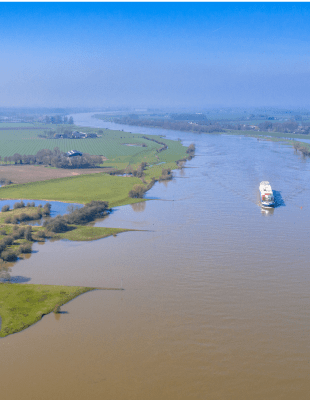 Scenic view of a boat sailing down a tranquil river, with trees lining the banks under a sunny sky.