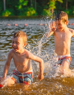Twee jongens rennen elkaar in het water achterna.