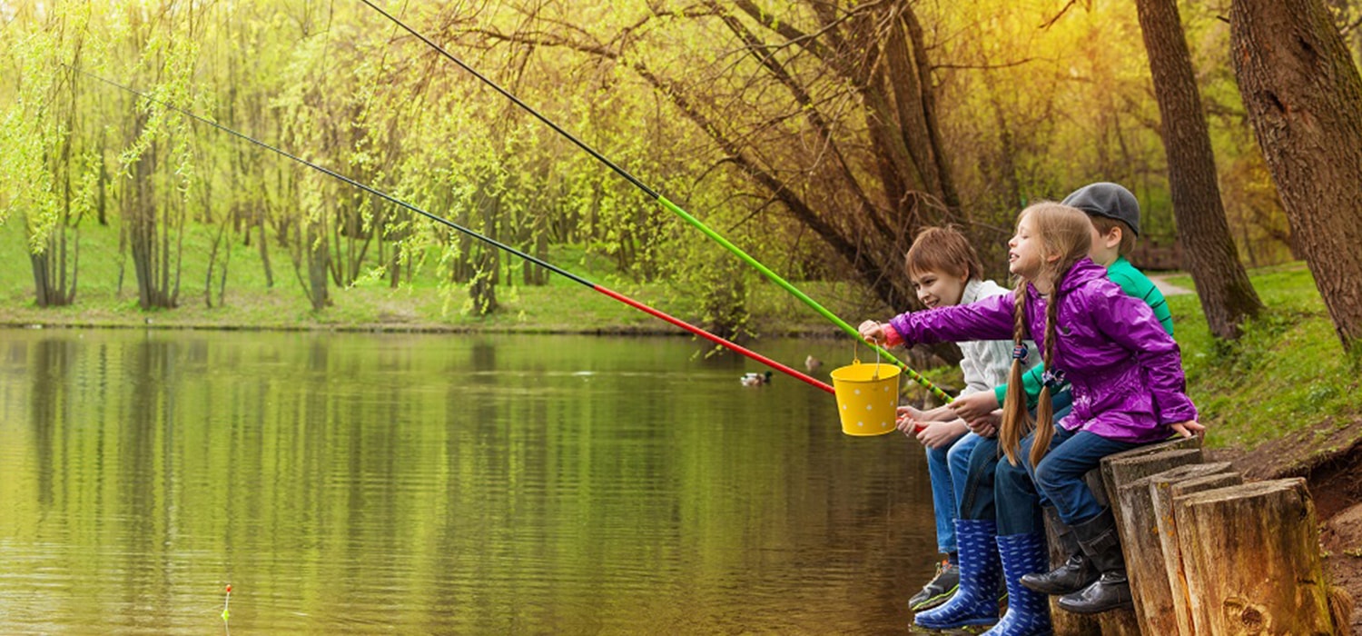 Drie kinderen die aan het vissen zijn aan de waterkant van een meertje.