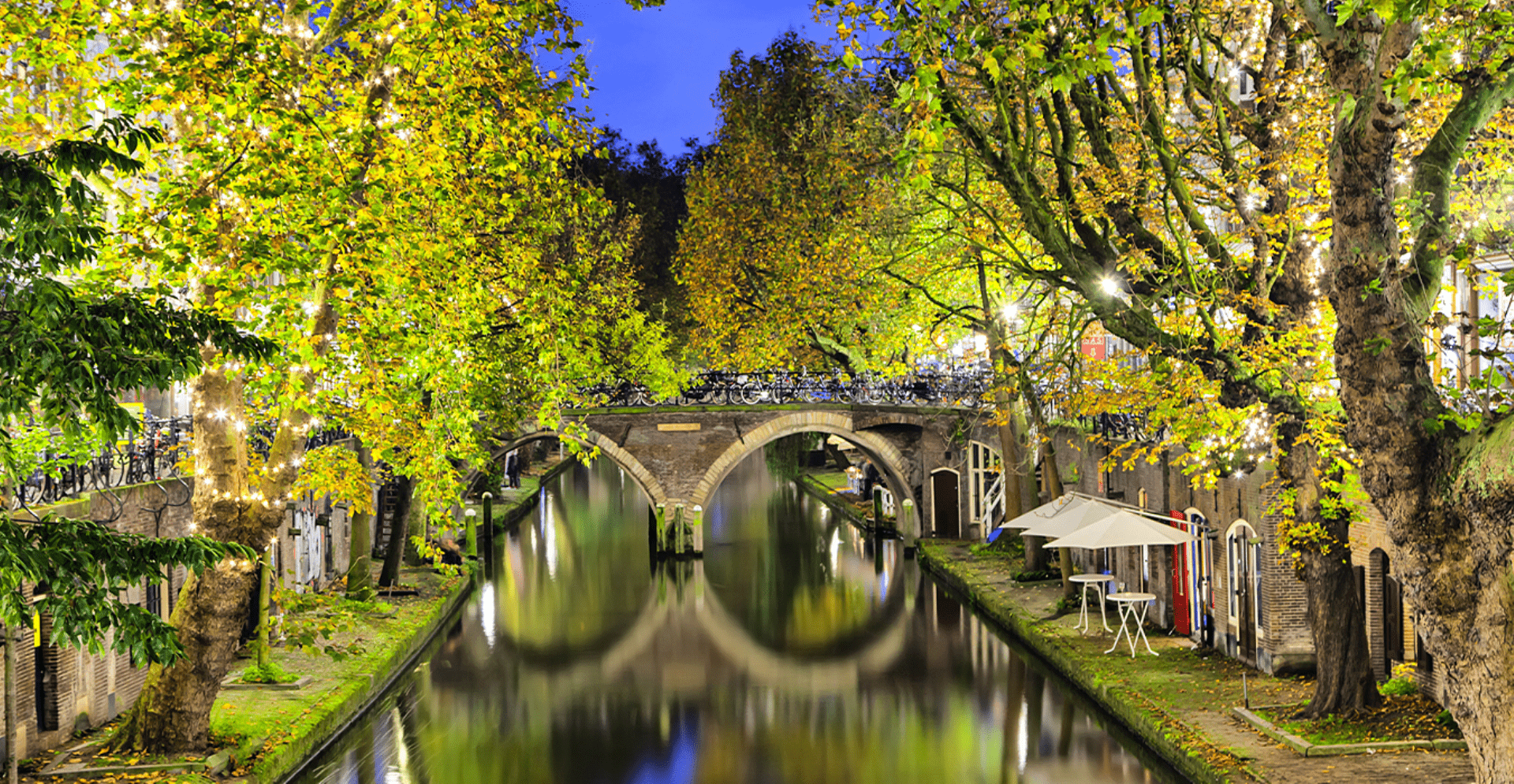 Bomenrij langs kanaal met terrassen en brug met bogen over het kanaal in Utrecht