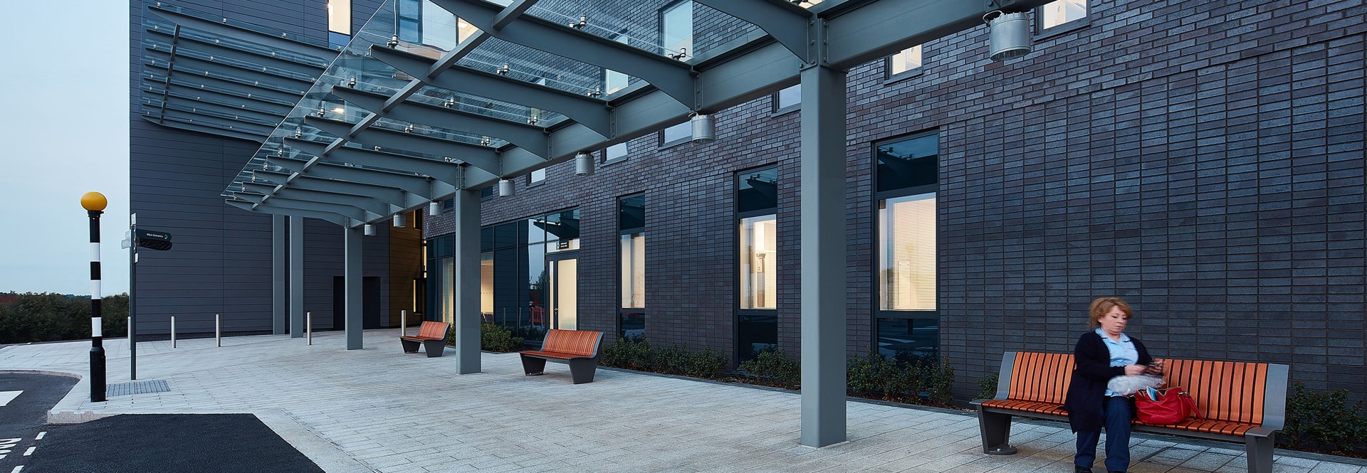A woman seated on a bench in front of a building, enjoying the outdoors in a serene environment.