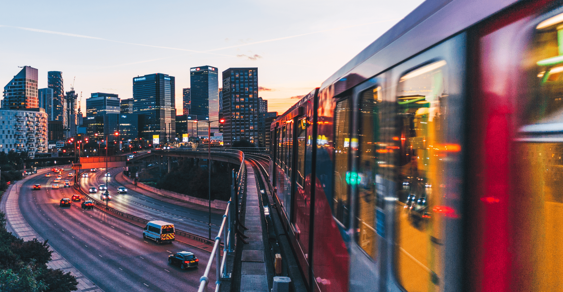 Moving train with the view of highway and buildings of the city.