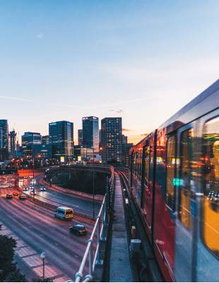 Moving train with the view of highway and buildings of the city.