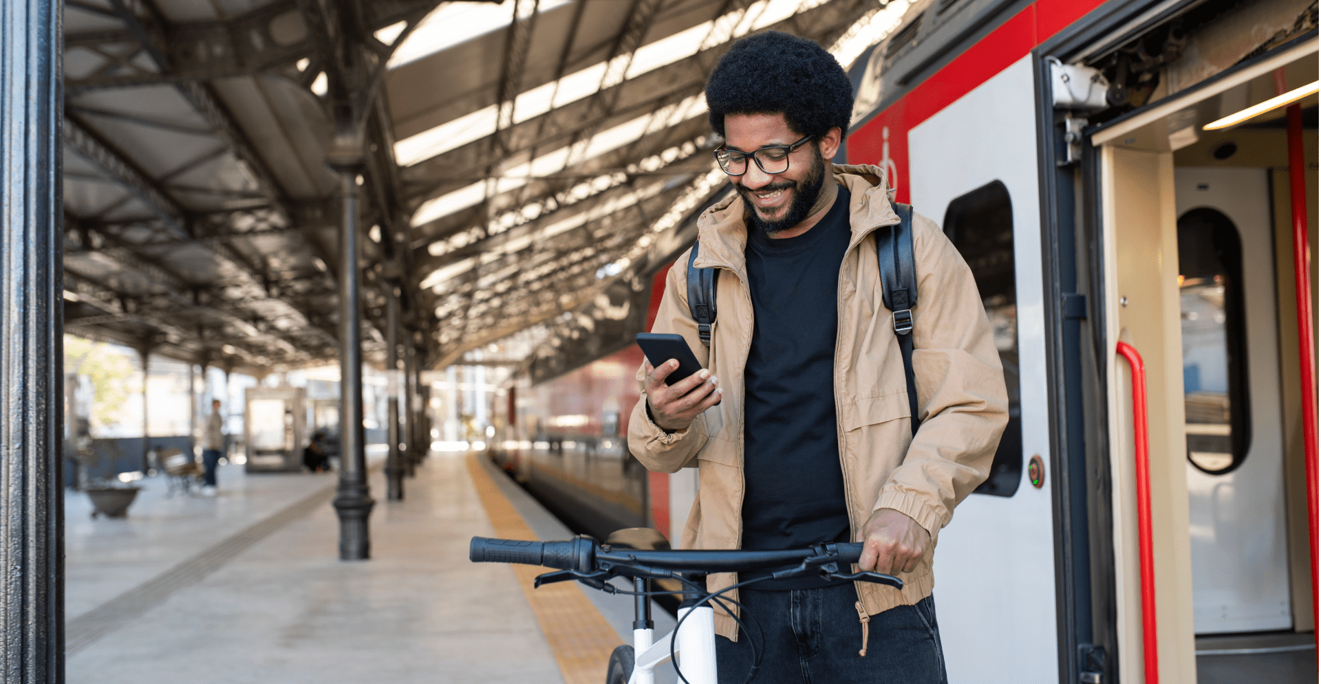 Smiling man using mobile phone standing by bicycle near train at station