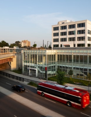A red bus travels along a highway beside a building under a clear sky.