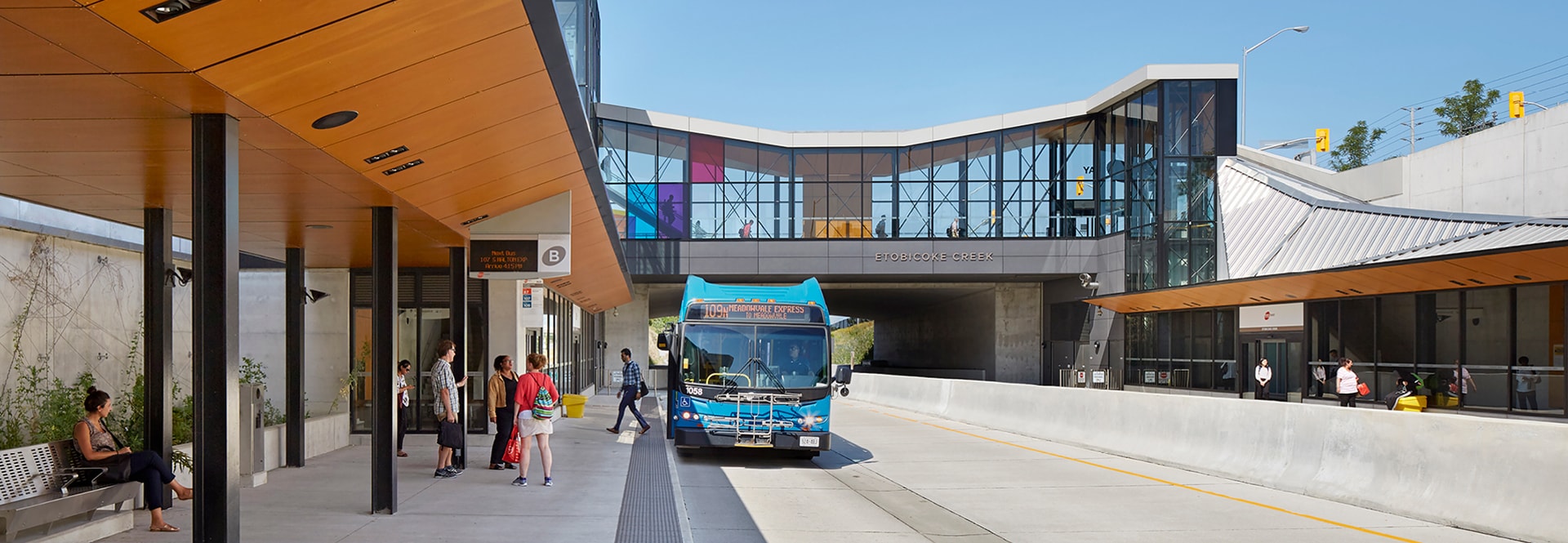 A bus is parked at a bus stop adjacent to a building, ready to pick up passengers.