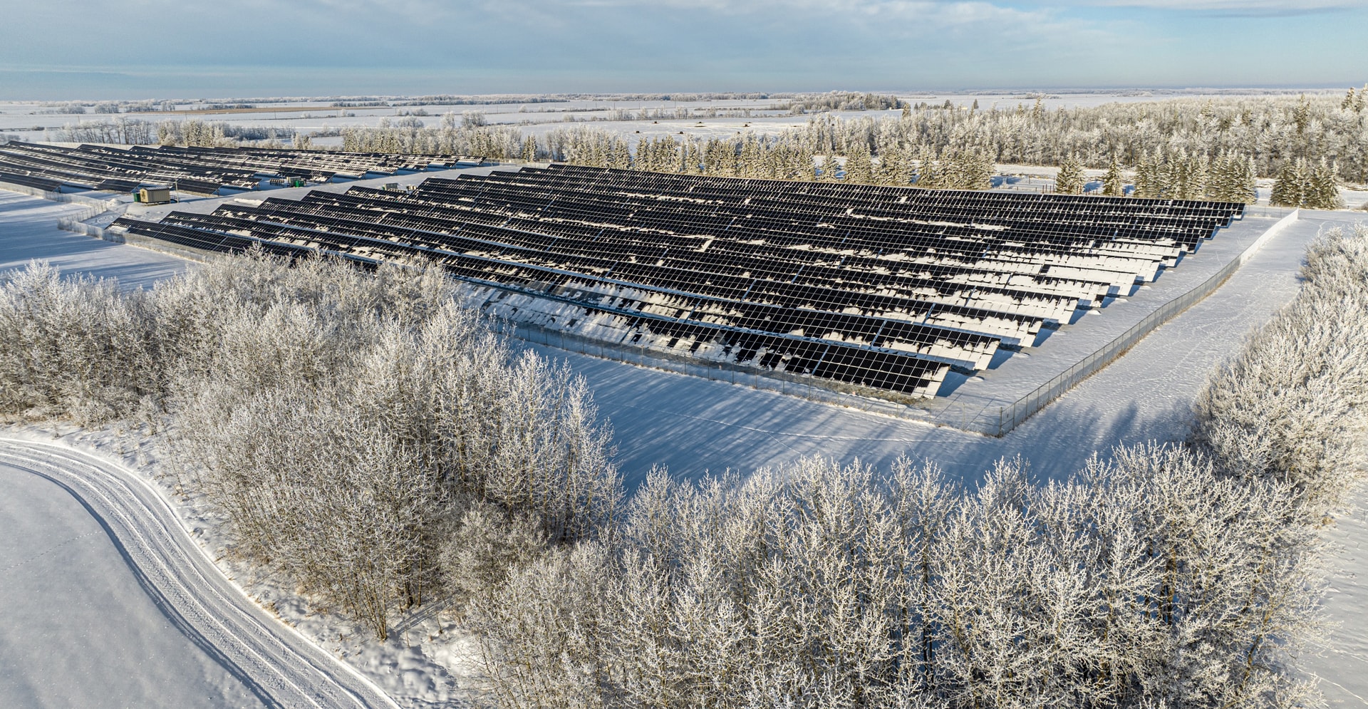 Aerial view of a solar farm covered in snow, showcasing rows of solar panels against a winter landscape.