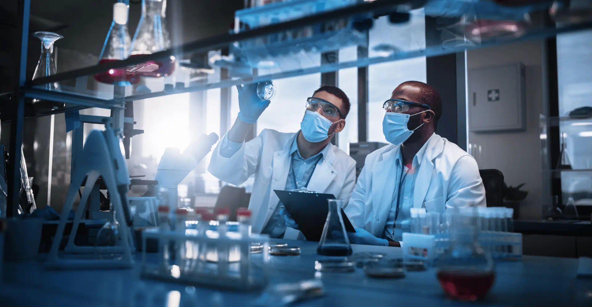 Two scientists wearing lab coats and masks while working on a research project.