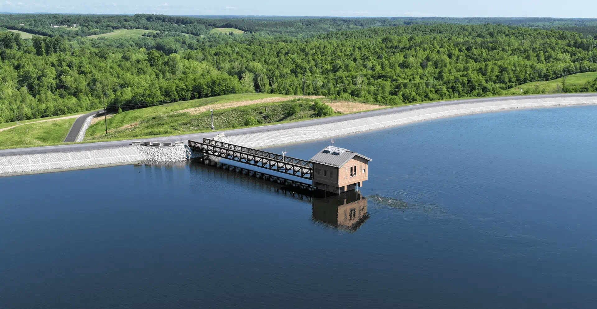 A dam on a serene lake, encircled by lush green trees, reflecting nature's tranquility.